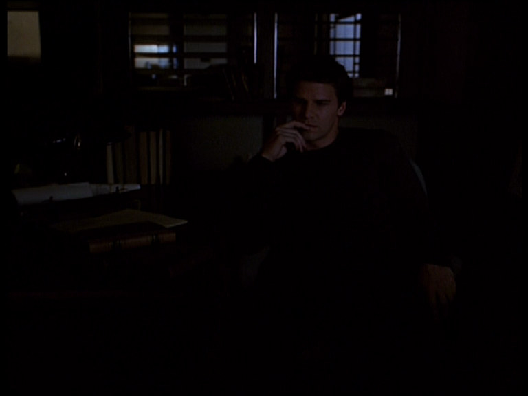 Angel sitting in a dark office, brooding.