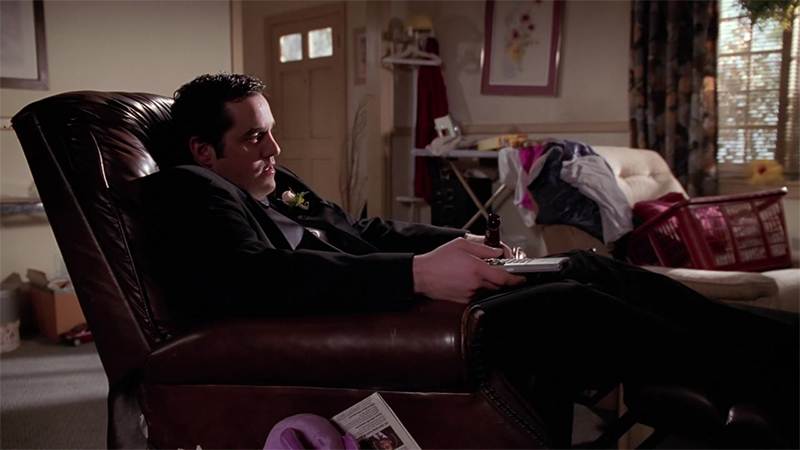 Xander sits on a chair holding a TV remote and a bottle of beer.