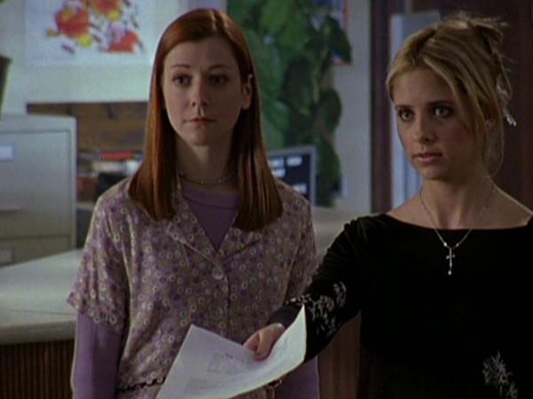 Buffy, standing next to Willow, hands a piece of paper to Giles.