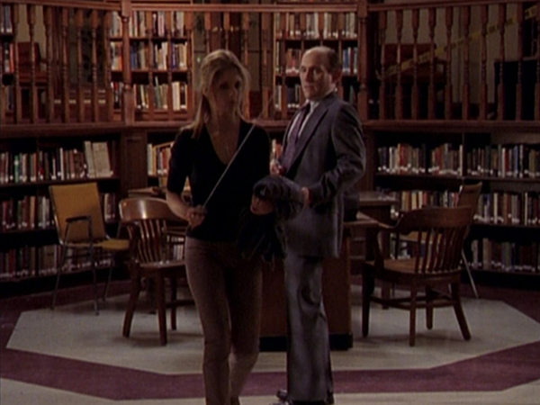 Buffy holds a sword aloft in the library, walking away from Principal Snyder.